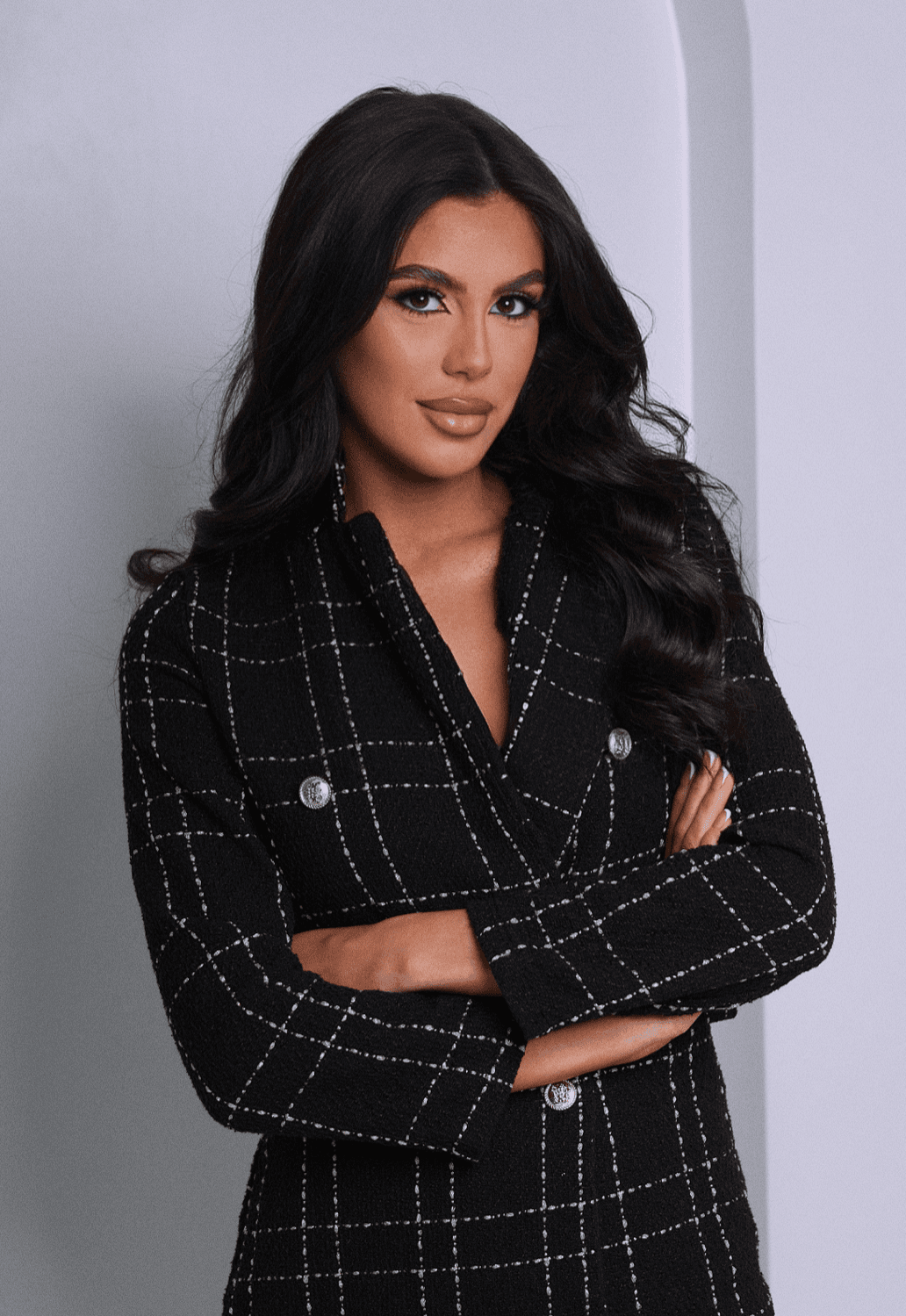 Woman with long dark hair wearing a black and white checkered tweed blazer, arms crossed.